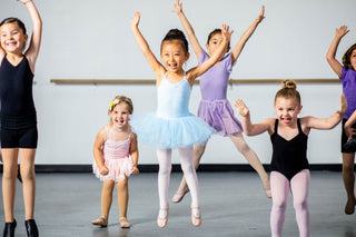 Happy young ballerinas in tutus and leotards smiling and practicing their dance moves